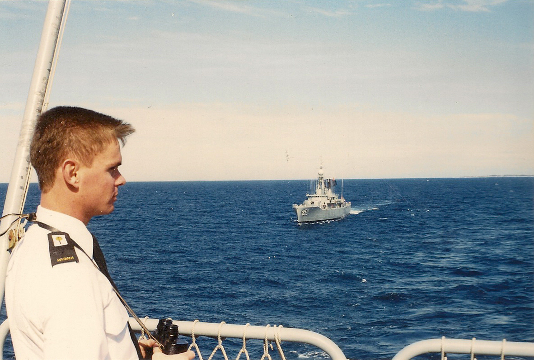 Lyle Holt as a young Royal Australian Navy officer on the bridge with binoculars, RAN warship in formation astern