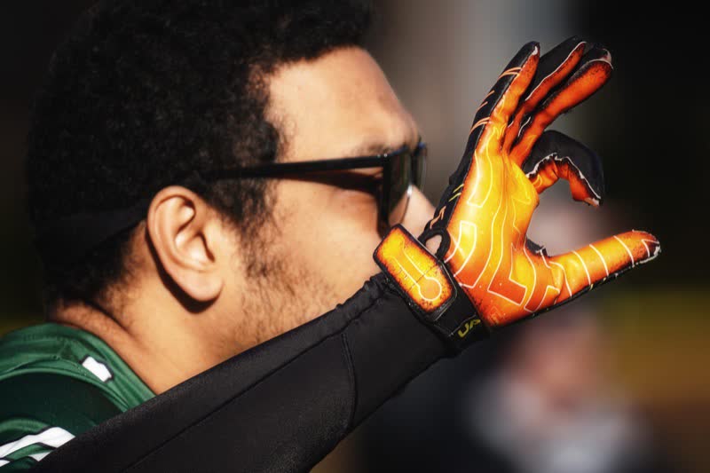 A flag football player in sunglasses holds up a hand in an orange patterned glove