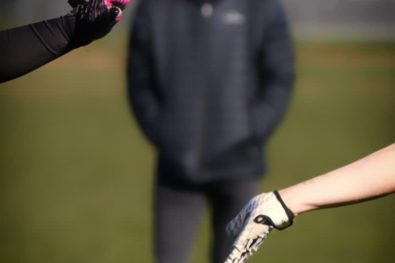 Two players' gloved hands reach towards each other, a blurred person in a dark jacket behind them