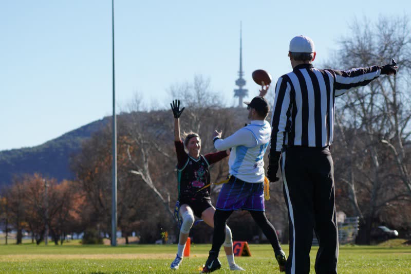 A flag football quarterback throws past a referee, with Telstra Tower on the hill behind