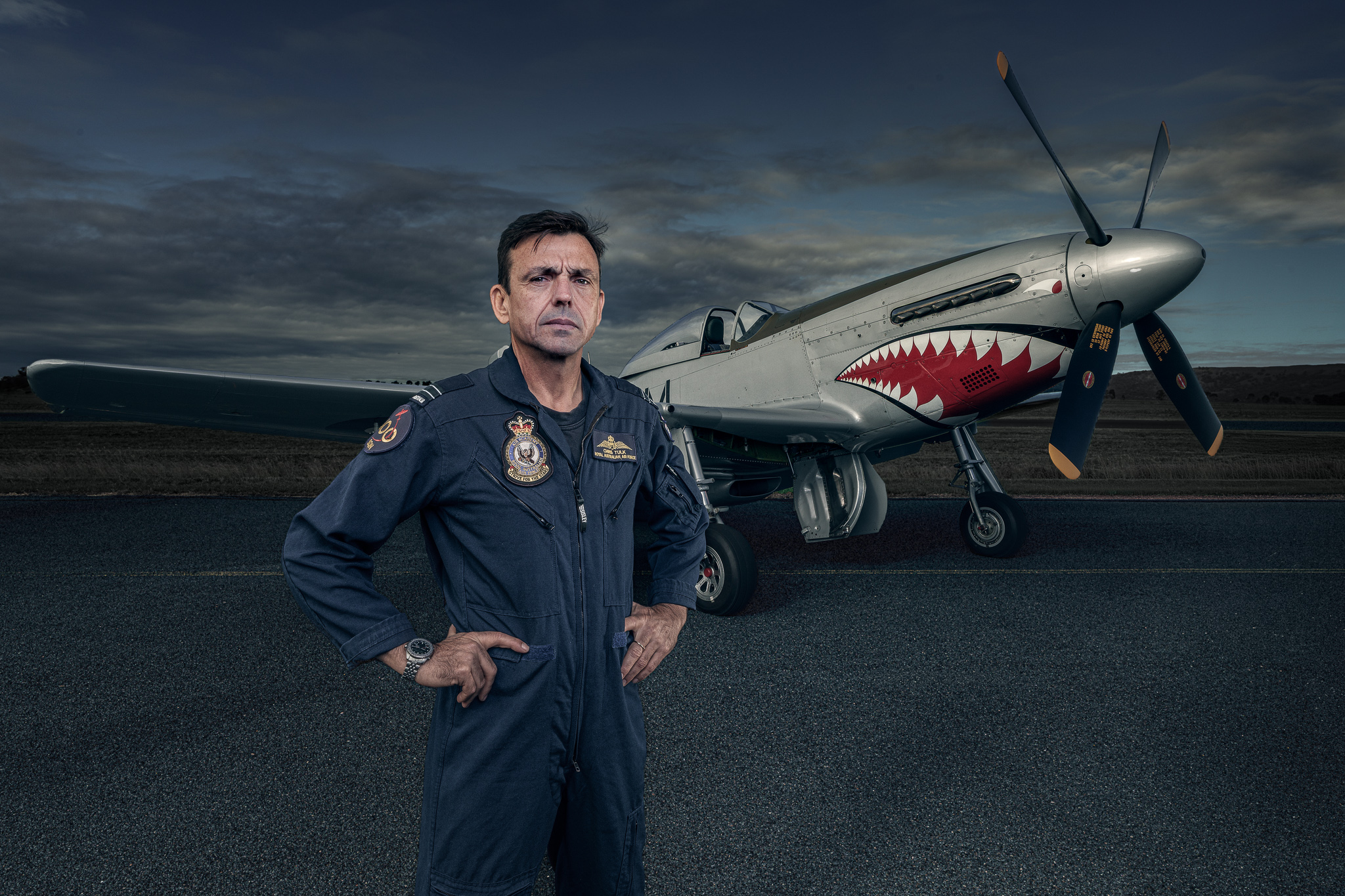 FLTLT Chris Tulk — full-length command portrait with P-51D Mustang AM-G, stormy sky